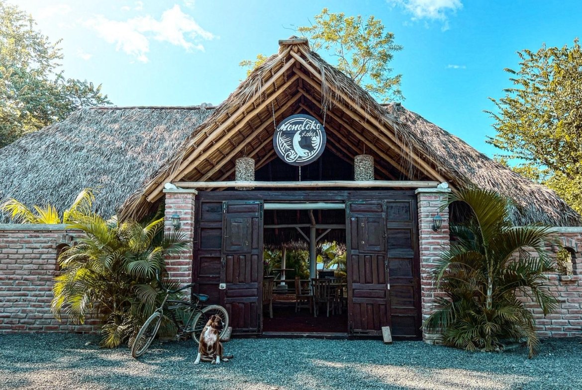 Large wooden entrance gate at Monoloko Lodge with the lodge dog waiting outside, near Playa Santana, Popoyo, Nicaragua