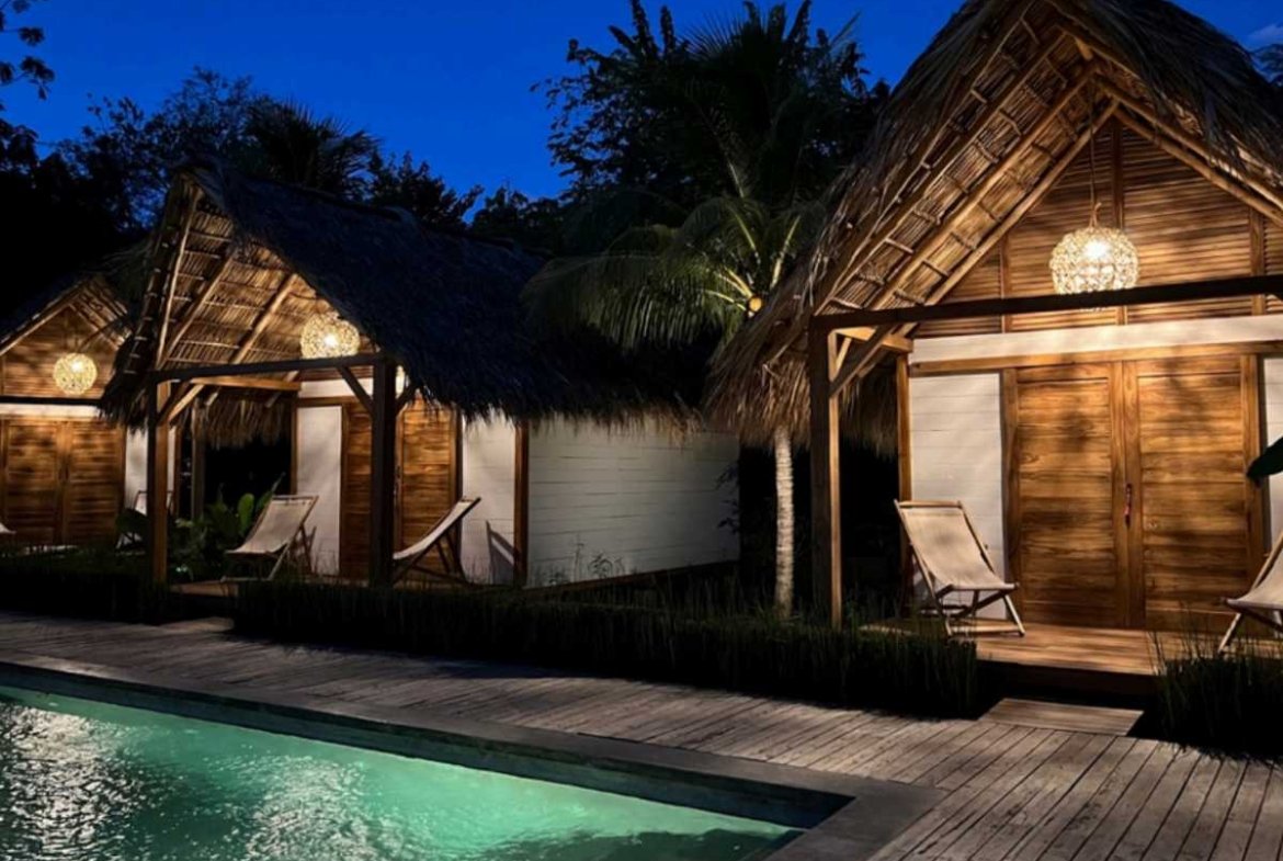 Wooden bungalows lit up at night at Monoloko Lodge, a surf lodge for sale near Playa Santana, Popoyo, Nicaragua