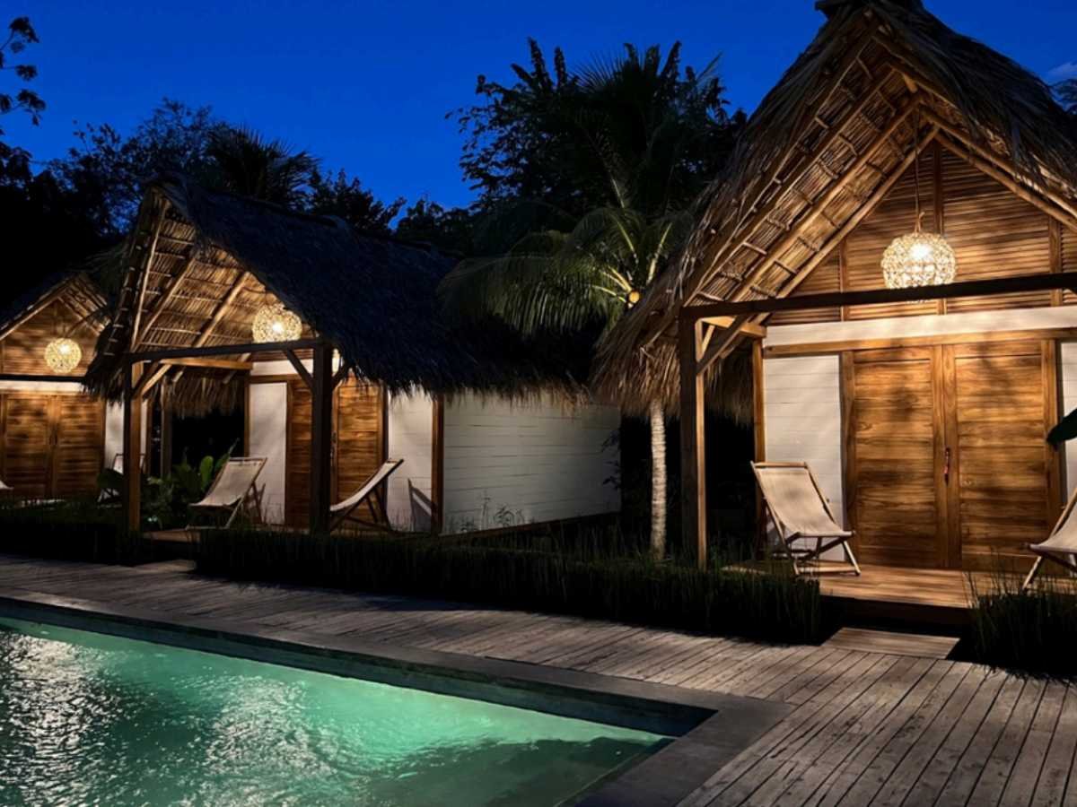 Wooden bungalows lit up at night at Monoloko Lodge, a surf lodge for sale near Playa Santana, Popoyo, Nicaragua