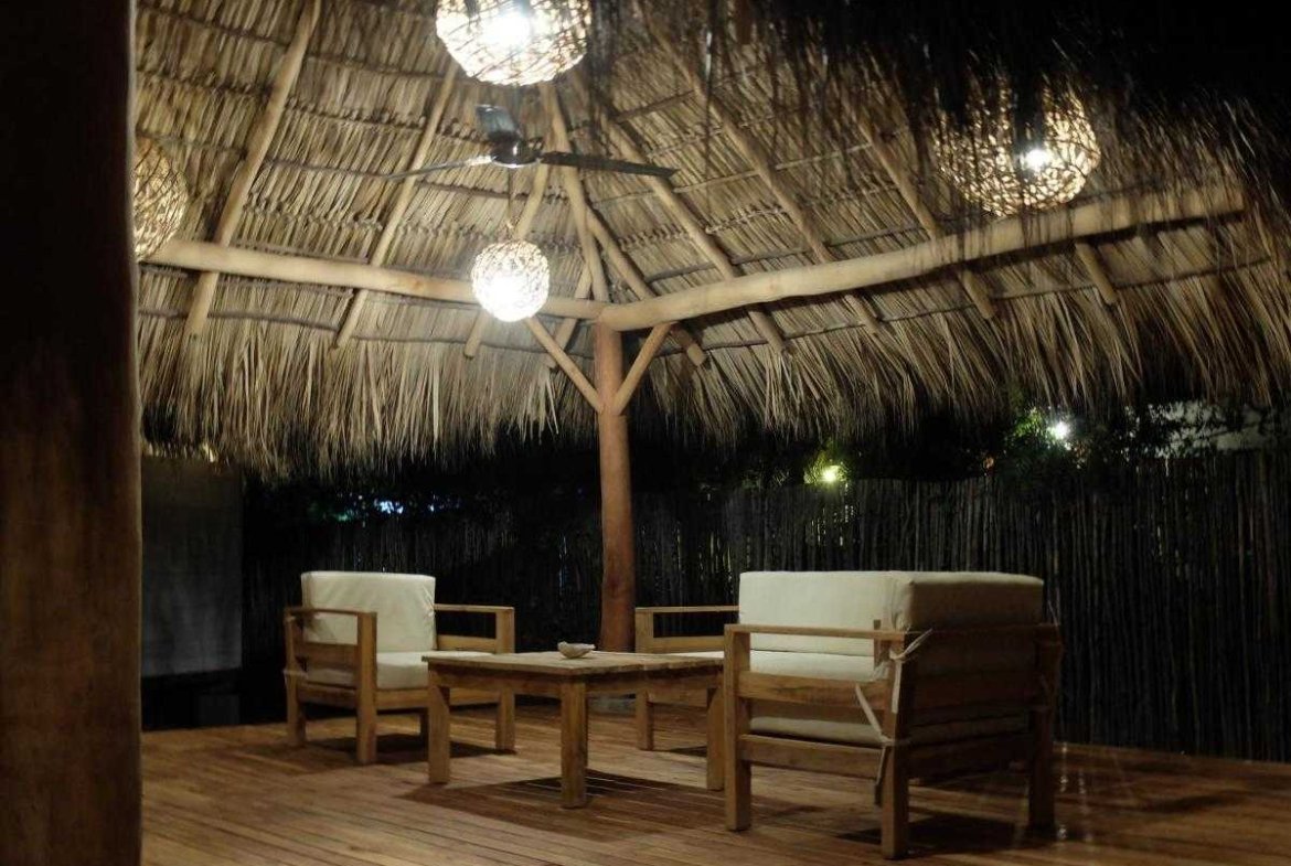 Wooden table and two lounge chairs under a thatched rancho at night at Monoloko Lodge, a turnkey surf lodge near Playa Santana, Popoyo, Nicaragua