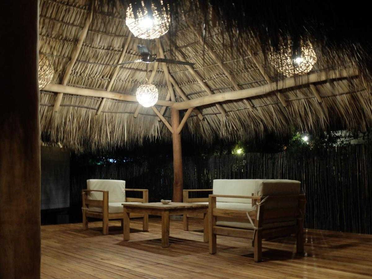 Wooden table and two lounge chairs under a thatched rancho at night at Monoloko Lodge, a turnkey surf lodge near Playa Santana, Popoyo, Nicaragua