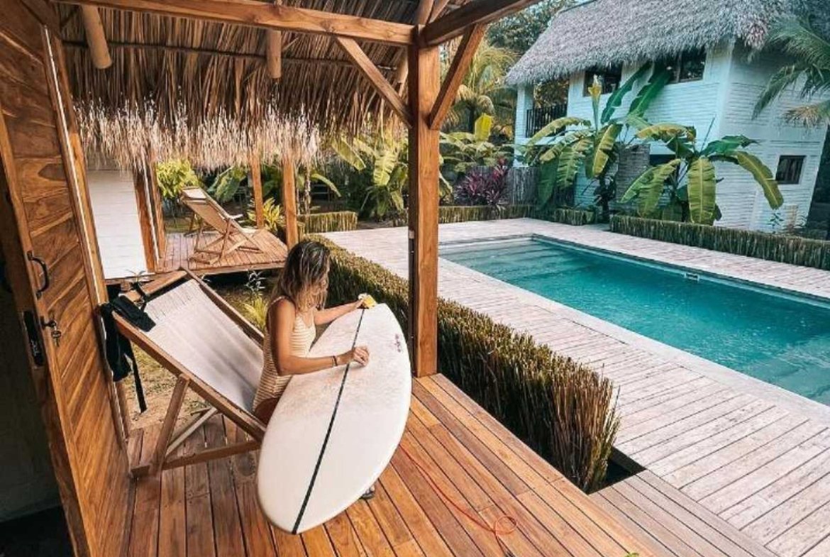 Surfer waxing her surfboard on the terrace overlooking the pool at Monoloko Lodge, near Playa Santana, Popoyo, Nicaragua