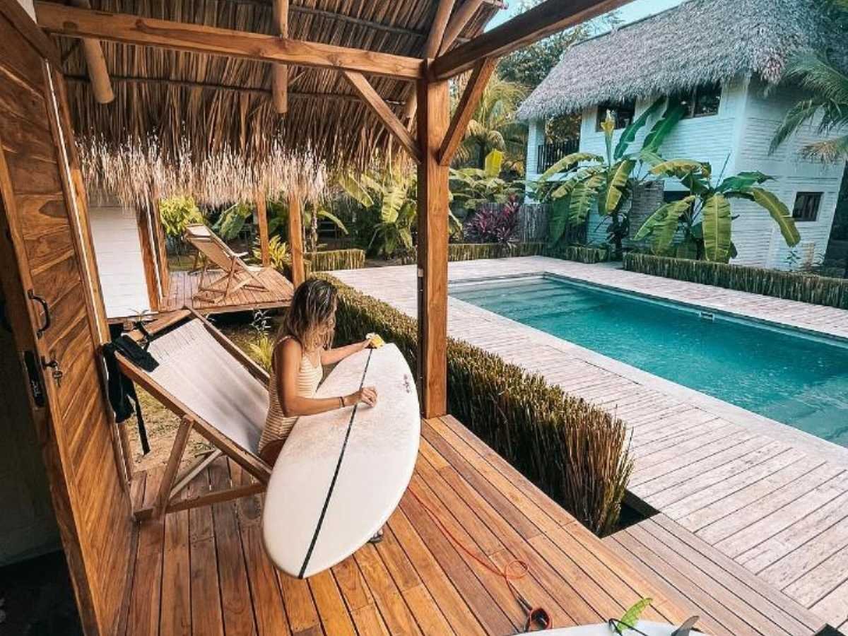 Surfer waxing her surfboard on the terrace overlooking the pool at Monoloko Lodge, near Playa Santana, Popoyo, Nicaragua